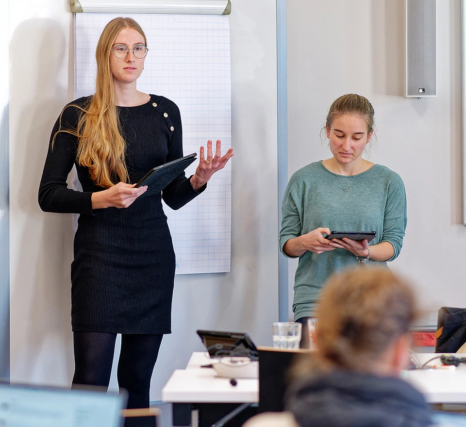 Zwei Studentinnen praesentieren etwas vor anderen 